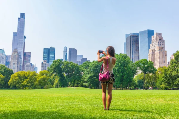 New York City woman tourist taking photo with phone of NYC Skyline in Sheep Meadow Central Park. Summer travel vacation landscape manhattan walk activity — Stock Photo, Image