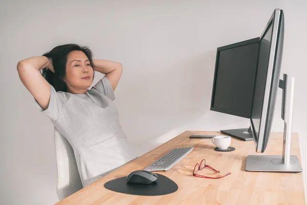 Работая дома, азиатская зрелая женщина отдыхает от удаленной работы в маленьком бизнесе за компьютерным столом, думая о досрочном выходе на пенсию или успехе онлайн-электронной коммерции. Китаянка средних лет, 50 лет. — стоковое фото