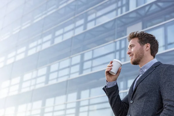 Happy young business professional man drinking coffee cup on his morning commute walk to work. Caucasian businessman with hot drink on office background looking away with satisfaction — Stock Photo, Image