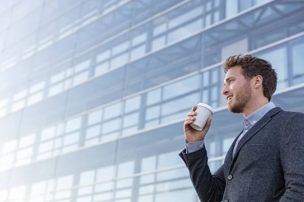 Buon giovane uomo d'affari professionale che beve una tazza di caffè sulla sua passeggiata pendolare mattutina al lavoro. uomo d'affari caucasico con bevanda calda su sfondo ufficio guardando lontano con soddisfazione — Foto Stock