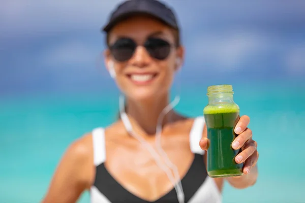 Healthy fit woman showing sports green juice smoothie drink for weight loss detox cleanse. Happy smiling athlete girl holding glass bottle drinking breafkast outside in summer outdoors — Stock Photo, Image