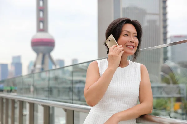 Phone Asian woman mature middle age chinese businesswoman talking business on mobile smartphone call outside on Shanghai street with Pearl tower in background. China travel — Stock Photo, Image