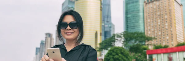 Teléfono asiático mujer madura que viaja con dispositivo móvil 5g en viaje de negocios viaje ciudad estilo de vida bandera panorámica. Elegante dama china con teléfono inteligente —  Fotos de Stock