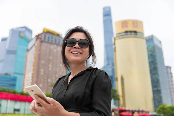 Asiatische Geschäftsfrau Immobilienmaklerin mit Handy-SMS in Shanghai City, China. Glücklich lächelnde ältere Dame arbeitet draußen am Smartphone — Stockfoto