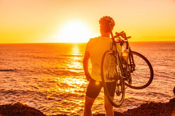 Triathlon road bike cyclist carrying bicycle watching sunset after outdoor race training by ocean coast landscape. Man athlete biking outdoors — Stock Photo, Image