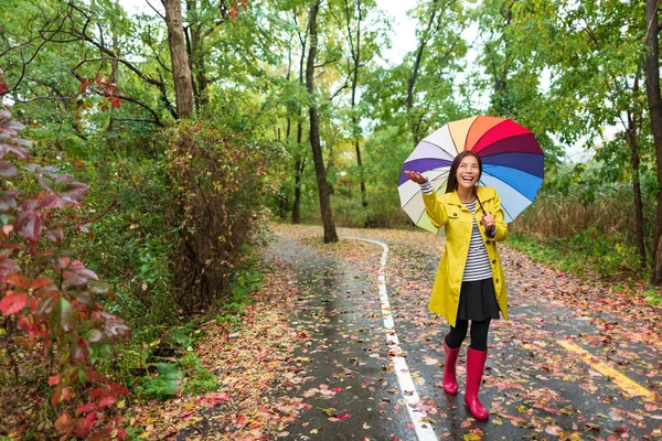 Asiatische Herbstfrau glücklich nach Regenspaziergang mit Regenschirm. Das weibliche Model blickt an einem regnerischen Herbsttag freudig in einem gelben Regenmantel draußen im Naturwald zum Himmel auf. Multiracial asiatische Mädchen — Stockfoto