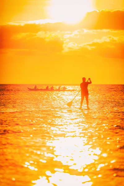 Hawaii ocean lifestyle - watersport activity on ocean - stand up paddleboard, people training on outrigger canoe. Vida saludable de verano activo. Silueta de persona de pie haciendo tabla de paddle —  Fotos de Stock