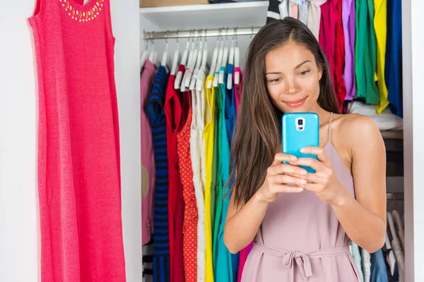 购物电话应用时尚女孩使用手机智能手机风格的衣服和选择服装衣柜。衣服衣柜里的年轻姑娘拿着自己的衣服做造型 — 图库照片