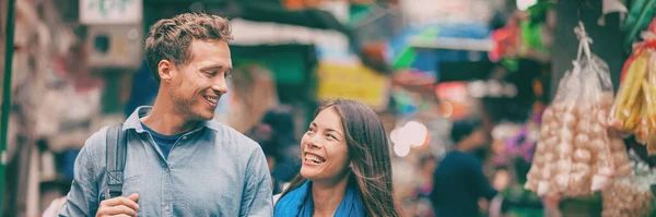 Turistas en el mercado callejero de Chinatown riendo juntos retrato panorámico de la bandera. Asia aventura de viaje, dos personas caminando visitando Hong Kong. Mujer joven, hombre enamorado — Foto de Stock