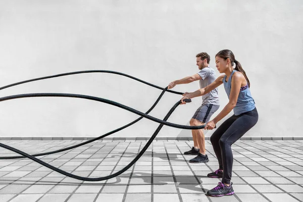 Spor salonunda sporcuların savaş halatlarıyla egzersiz yapması. Kadın ve erkek çift birlikte idman yapıyor. İp egzersizi yapıyor. Kollarını ve kardiyosunu çalıştırıyor. — Stok fotoğraf