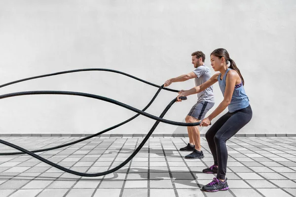 Fitnessmenschen, die im Fitnessstudio mit Kampfseilen trainieren. Frau und Mann trainieren gemeinsam beim Seiltraining, bei dem Arme und Herz für Crossfit-Übungen trainiert werden — Stockfoto