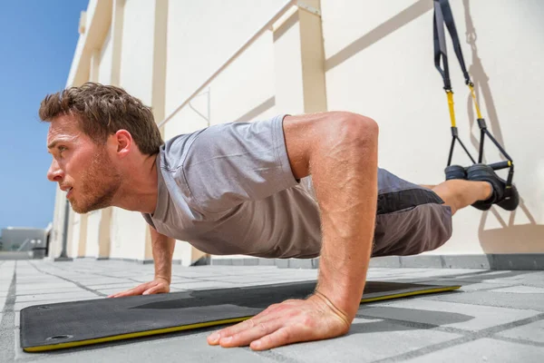 Hombre de fitness haciendo flexiones usando correas de suspensión en el gimnasio. Atleta haciendo ejercicios push-up de peso corporal en el suelo al aire libre — Foto de Stock