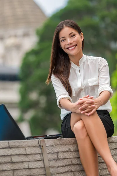 Glückliche asiatische junge Frau, die während der Arbeitspause im Stadtpark in die Kamera lächelt und draußen sitzt. Porträt eines chinesischen kaukasischen Mädchens in ihren Zwanzigern im Büro draußen, Hongkong, China, Asien — Stockfoto