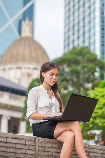 香港のビジネス街の画面を見て外で働いているコンピュータのラップトップを持つビジネス女性。若い女性プロの実業家が屋外に座っている。アジア系中国人白人女性 — ストック写真