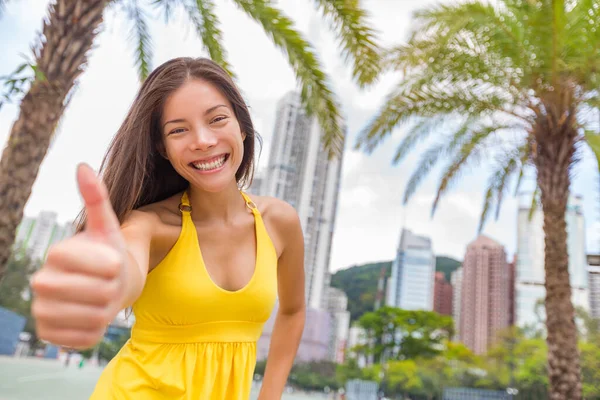 Ευτυχισμένο κινέζικο κορίτσι κάνει αντίχειρες επάνω στην ικανοποίηση στην πόλη του Χονγκ Κονγκ, Ασία Κίνα ταξιδιωτικό τρόπο ζωής. Νεαρή χαμογελαστή πολυφυλετική — Φωτογραφία Αρχείου