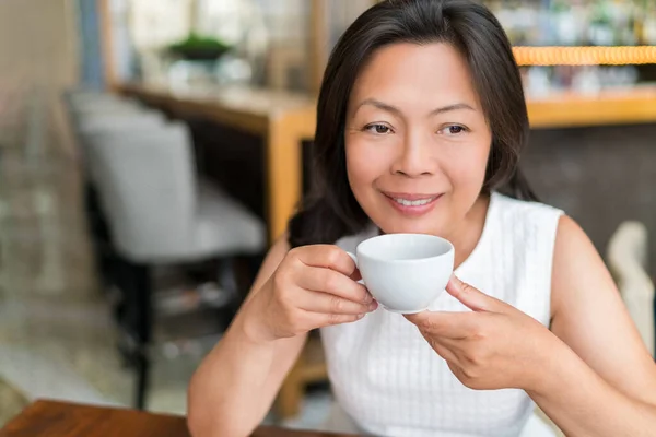 Зрелая азиатка пьет английский чай на завтрак, расслабляясь в кафе. Китайская женщина среднего возраста наслаждается городским образом жизни, стильной жизнью — стоковое фото