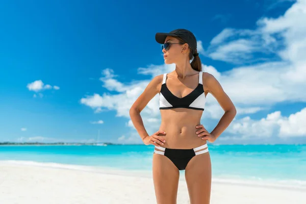 Αθλητική γυναίκα στην παραλία έτοιμη για την καλοκαιρινή περίοδο. Bikini fitness γυναίκα με καπέλο αντηλιακής προστασίας και γυαλιά ηλίου μαύρισμα που δείχνει το σώμα απώλειας βάρους στις διακοπές — Φωτογραφία Αρχείου