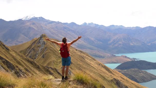 Res vandrare tittar på utsikten över berg sjö natur landskap på Nya Zeeland på berömda Wanaka vandring till Roys Peak. Vandrare njuter av fantastisk natur på Nya Zeeland fridfull och nöjd med armarna upp. — Stockvideo