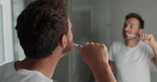 Escovar os dentes homem olhando no espelho do banheiro em casa usando escova de dentes — Vídeo de Stock