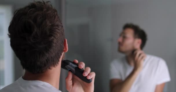 Sakalını elektrikli tıraş makinesi kullanarak tıraş eden bir adam. Erkek güzellik tımar konsepti. — Stok video