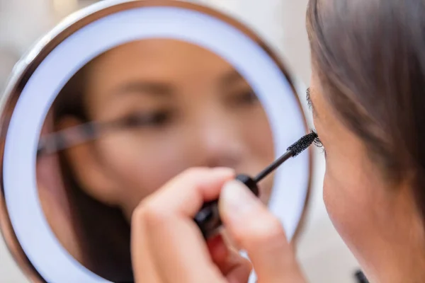 Frau steckt Wimperntusche in beleuchteten Schminkspiegel — Stockfoto