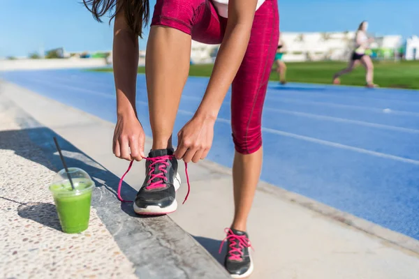 Koşan kadın ayakkabılarını bağlıyor yeşil smoothie içiyor — Stok fotoğraf