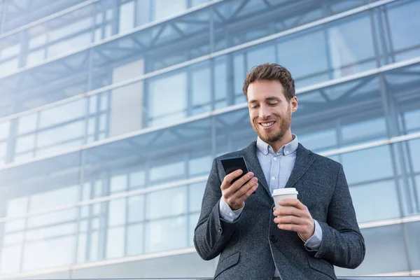 Businessman holding mobile cell phone using app texting sms message wearing suit. Young urban professional man using smartphone at office building — Stock Photo, Image