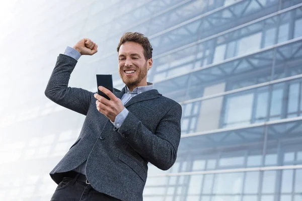 Успешный бизнесмен выигрывает в приложении для мобильных телефонов. Подбадривание бизнесмена, глядя на смартфон онлайн игровой вызов или сделки на работе — стоковое фото