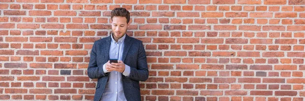 Affärsman sms SMS telefon app i city street på tegelvägg bakgrund. Affärsman som håller smartphone i smarta casual wear stående. Ung yrkeslivsstil i städerna — Stockfoto