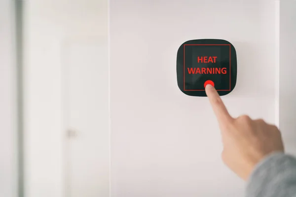 スマートホームデジタルサーモスタットタッチスクリーンは、夏の熱波のストロークに熱警告温度を表示します。リビングルームの壁にエアコンの温度を調整するためにタッチスクリーンに触れる女性 — ストック写真