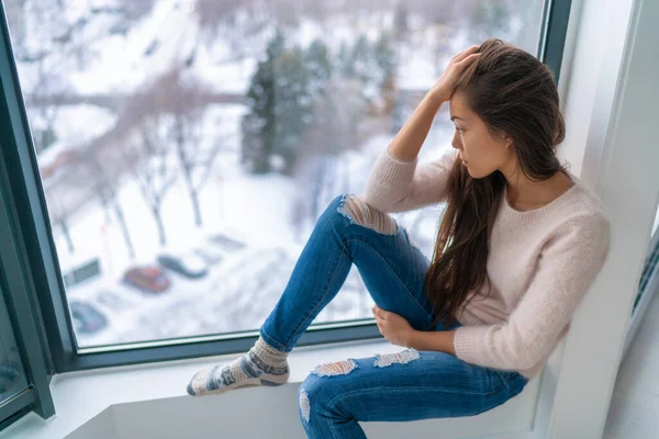 Hiver déprimé fille triste solitaire par la fenêtre de la maison en regardant le froid bouleversé malheureux. Mauvais sentiments stress, anxiété, chagrin, émotions. Portrait de femme asiatique — Photo