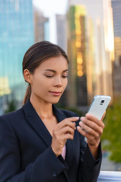 Ασιάτισσα επιχειρηματίας που στέλνει μηνύματα στο κινητό της, κοιτάζοντας την ηλεκτρονική τραπεζική στη δουλειά. Κτίρια γραφείων άνθρωποι της πόλης με κοστούμια. Κινέζα επιχειρηματίας χρησιμοποιώντας smartphone με το χέρι — Φωτογραφία Αρχείου
