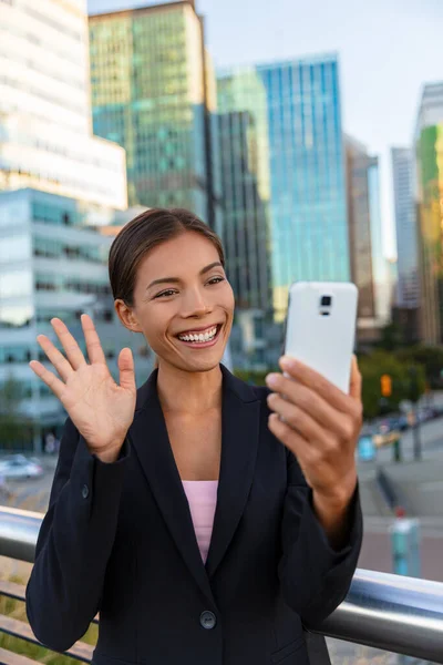 People on video call saying hello waving at camera. Asian woman video calling business partner on smartphone online in city street - Office buidlings on videochat call. Selfie entrepreneur cellphone — Stock Photo, Image