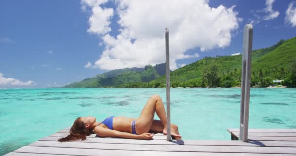 Lüks tatil beldesi bikinili kadın deniz aşırı bungalovda güneşleniyor. — Stok video