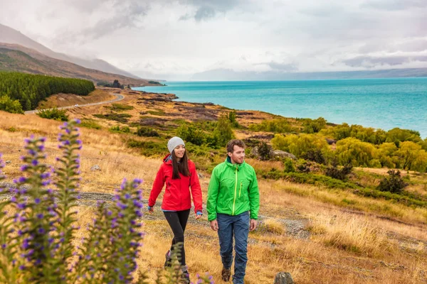 Viaje a Nueva Zelanda: un par de turistas que caminan en la naturaleza con vistas al lago Pukaki cerca de Aoraki, también conocido como Monte Cook, en el mirador de Peters, un famoso destino turístico — Foto de Stock
