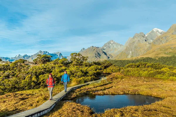 Caminhadas na Nova Zelândia. Jovem casal caminhando na trilha em Routeburn Track durante o dia ensolarado. Caminhantes estão carregando mochilas enquanto pisam Key Summit Track no Fiordland National Park, na Nova Zelândia — Fotografia de Stock
