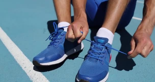 Бігун-спортсмен готується до бігу зав'язати шнурки на біговій доріжці стадіону — стокове відео