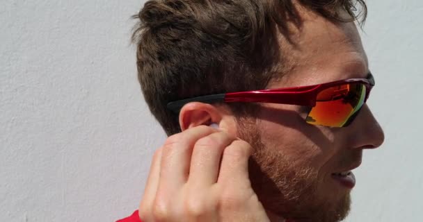 Joven poniéndose auriculares inalámbricos corriendo usando gafas de sol deportivas — Vídeo de stock