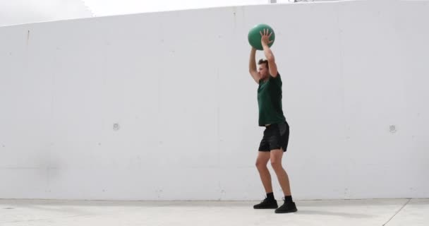 Squat with overhead medicine ball shoulder press. Weight exercises workout fitness man training legs and glutes with weighted medicine ball squats. Athlete working out at gym — Stock Video