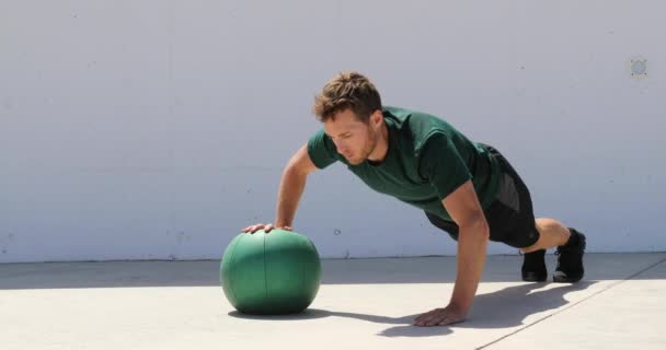 Fitness Man δύναμη προπόνηση pushup στήθος και ώμου μυς κάνει εναλλασσόμενο single βραχίονα ιατρική μπάλα push-ups πάτωμα ασκήσεις σε υπαίθριο γυμναστήριο — Αρχείο Βίντεο