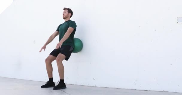 L'homme d'entraînement de force faisant des squats en utilisant le roulement de balle de médecine sur le mur accroupi au centre de remise en forme. Exercice squat exercices de poids corporel à l'aide de médecine ball. Fitness athlète travailler — Video