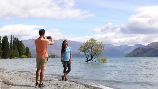 Новозеландские туристы фотографируют одинокое дерево Ванака на озере — стоковое видео