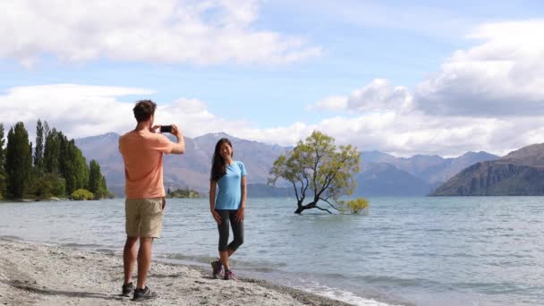 Turistas neozelandeses toman fotos telefónicas de Wanaka Lone Tree en el lago — Vídeo de stock