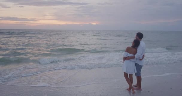 Luna de miel pareja relajándose en la playa mirando la puesta de sol abrazándose en el amor — Vídeo de stock