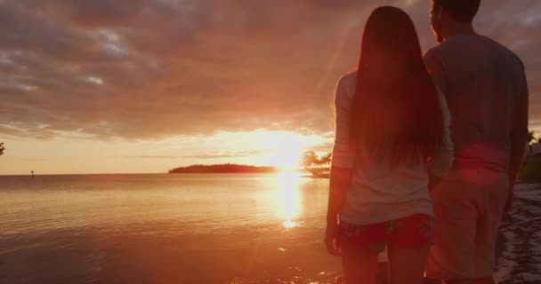 Sevgili balayı çifti turuncu gün batımında sahilde yürüyor. — Stok video
