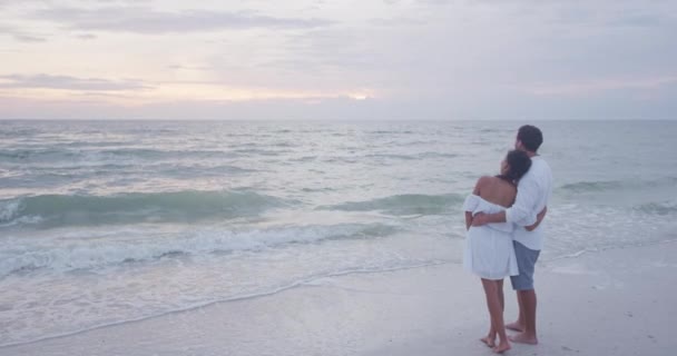 Casal de lua de mel romântico relaxante na praia olhando para o pôr do sol abraçando no amor — Vídeo de Stock