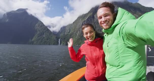 Para bawiąca się robieniem selfie video za pomocą smartfona na statku wycieczkowym, Milford Sound, Fiordland National Park, Nowa Zelandia. Wielokulturowa para uśmiecha się śmiejąc się na wakacjach — Wideo stockowe