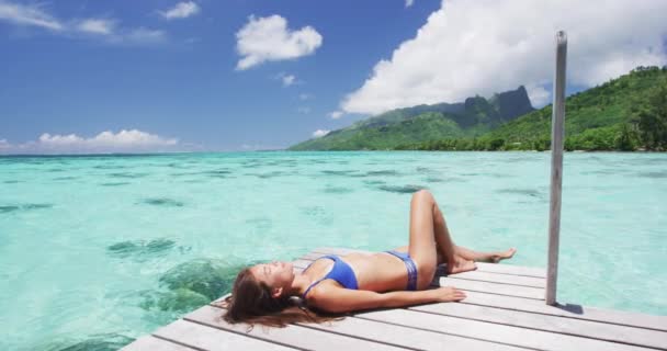 Lüks tatil beldesi bikinili kadın deniz aşırı bungalovda güneşleniyor. — Stok video