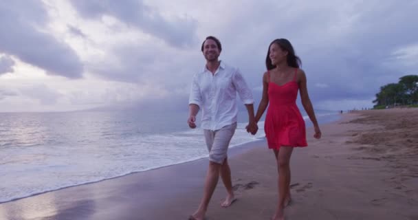 Miesiąc miodowy namiętna para trzymająca się za ręce spacerując po plaży — Wideo stockowe