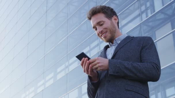 Empresario SMS mensajes de texto utilizando la aplicación en el teléfono inteligente en el distrito de negocios de la ciudad — Vídeo de stock